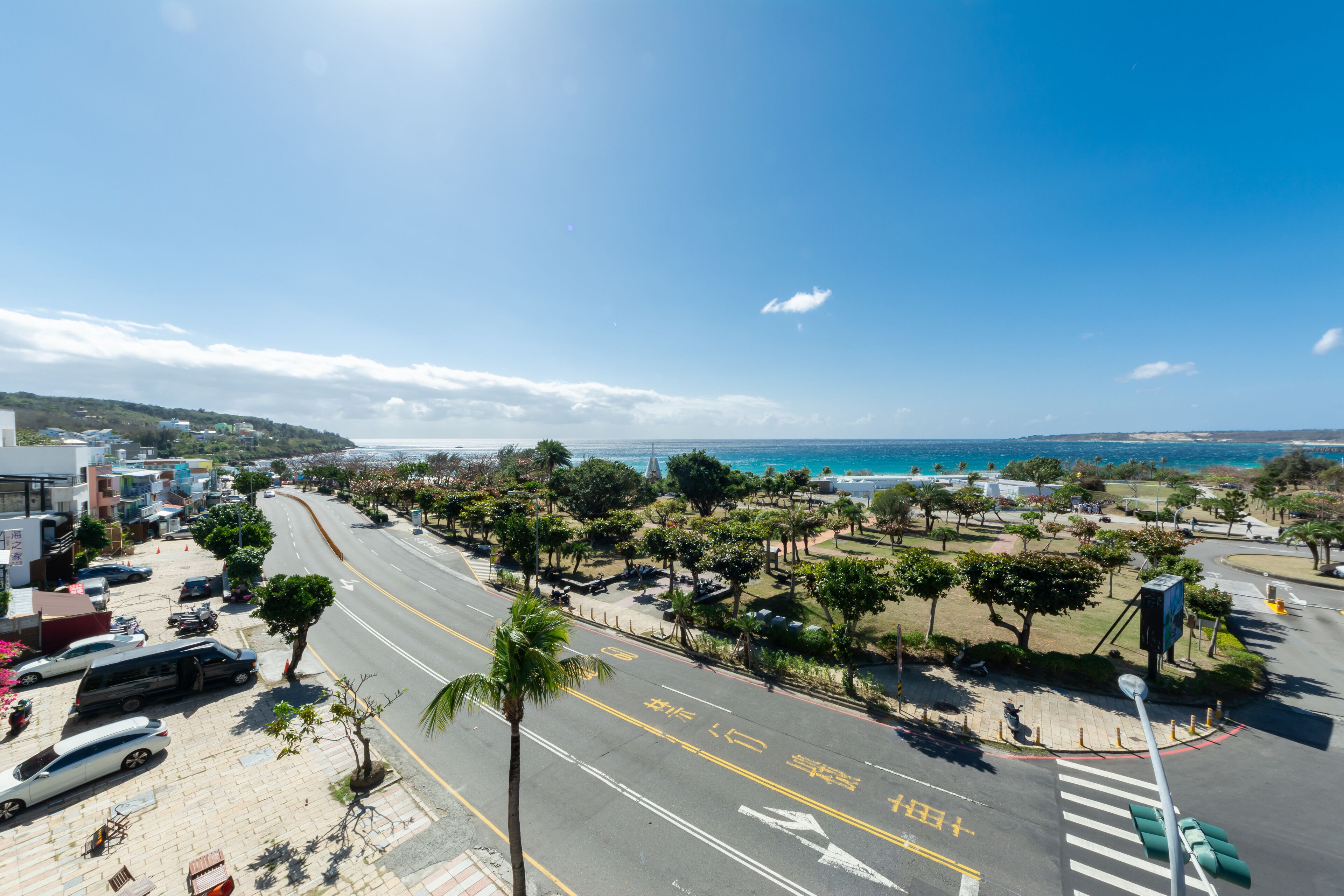 Eine Küstenstraße mit Zebrastreifen, Palmen und Blick auf das Meer.