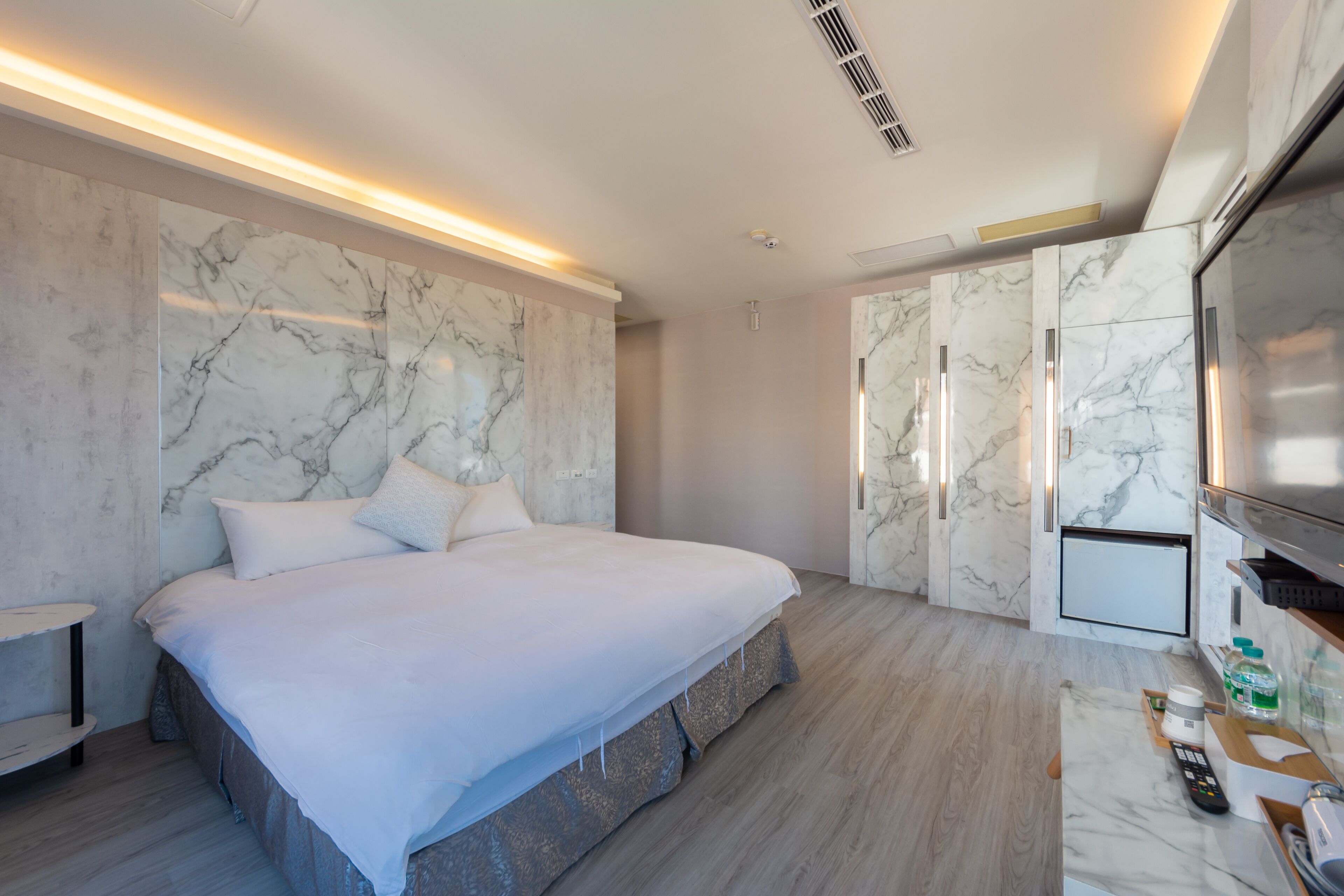 Una habitación de hotel moderna con una cama grande, paredes de mármol, un televisor de pantalla plana y un minibar.