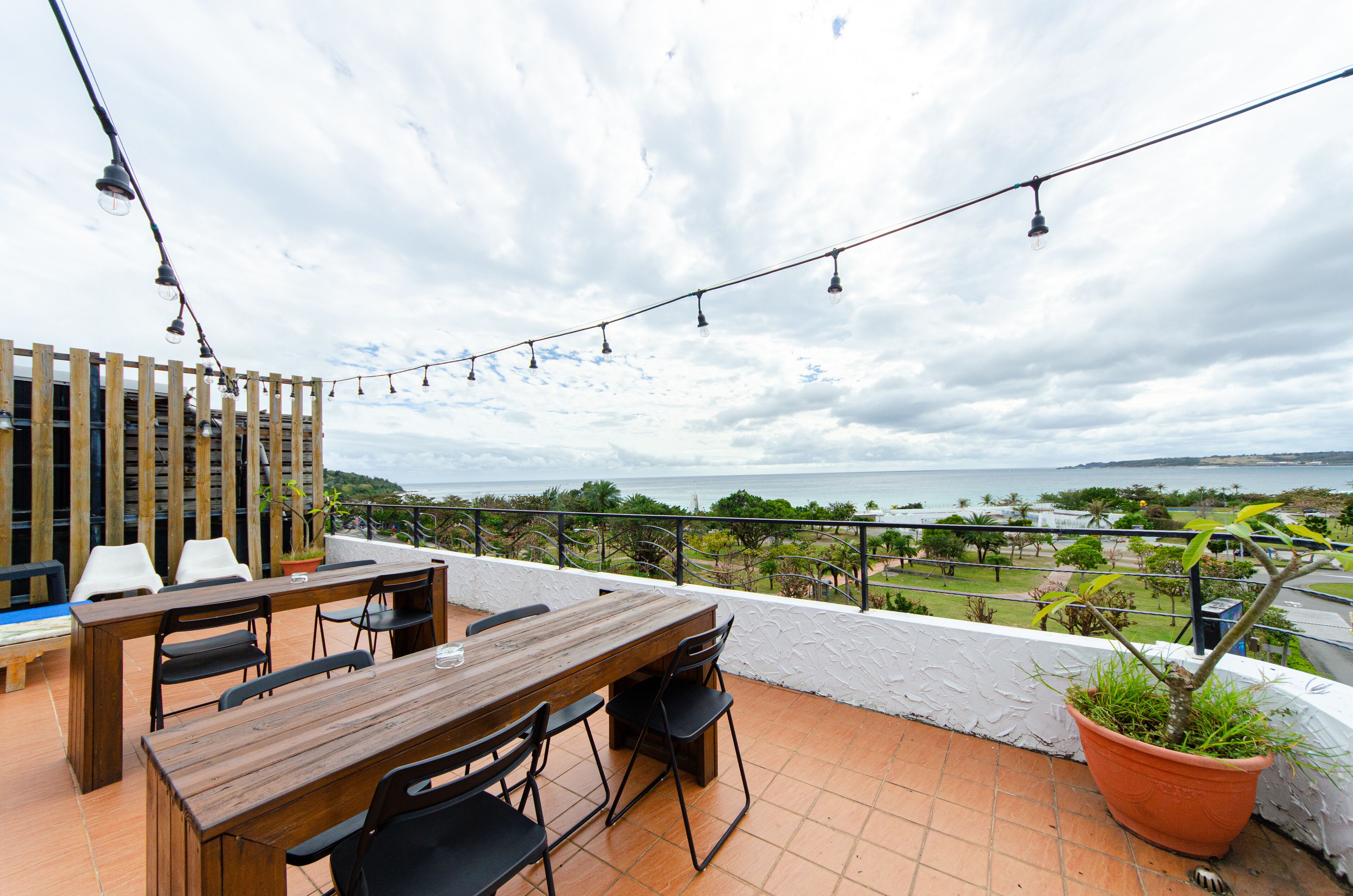 A terrace with a wooden table and chairs, a potted plant, and a view of the sea.