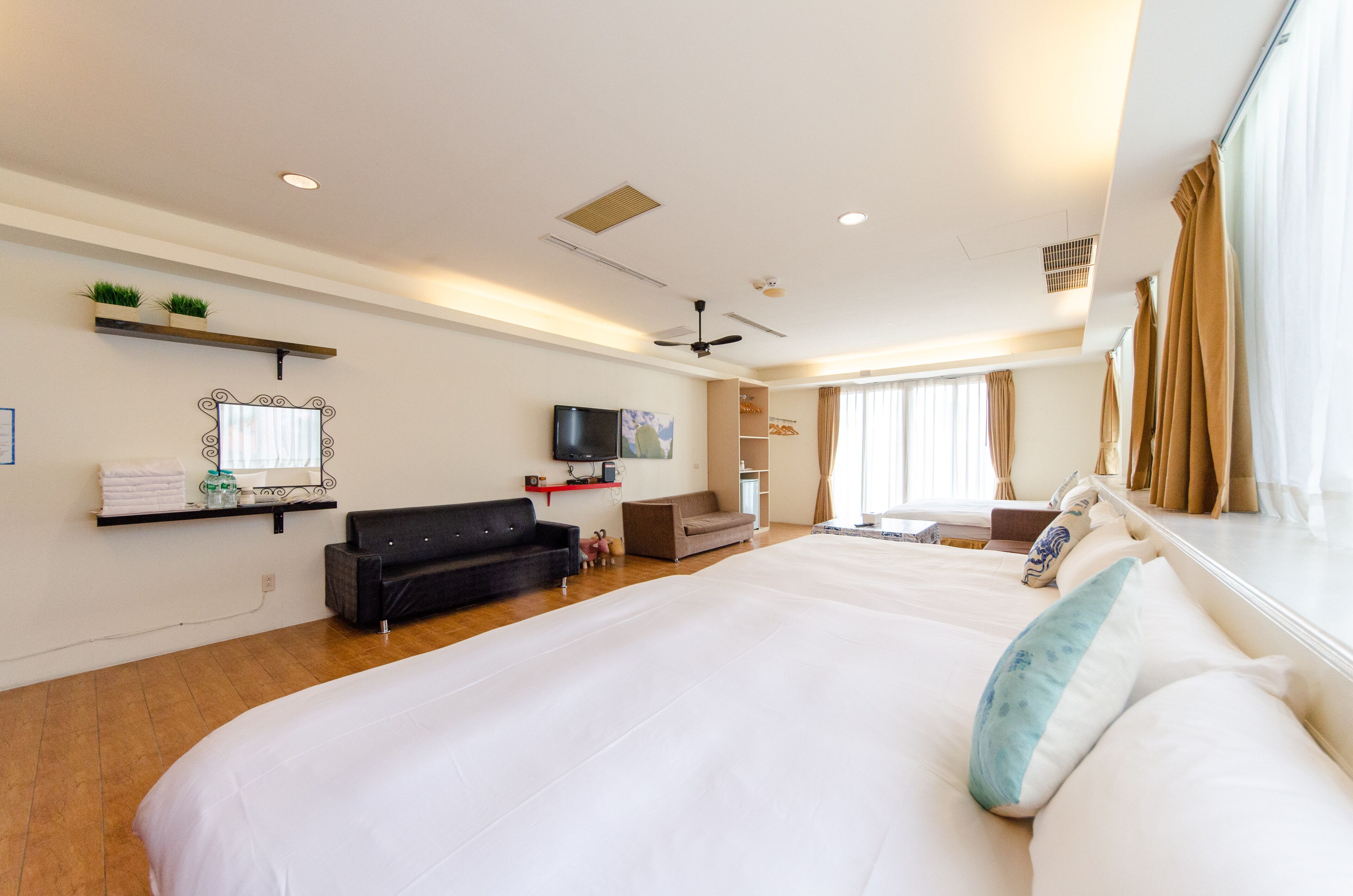 Amplia habitación de hotel con una cama grande, televisión de pantalla plana, ventilador de techo y ventana con cortinas.