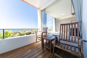 Un balcón con mobiliario de madera, vista al océano y barandilla blanca.