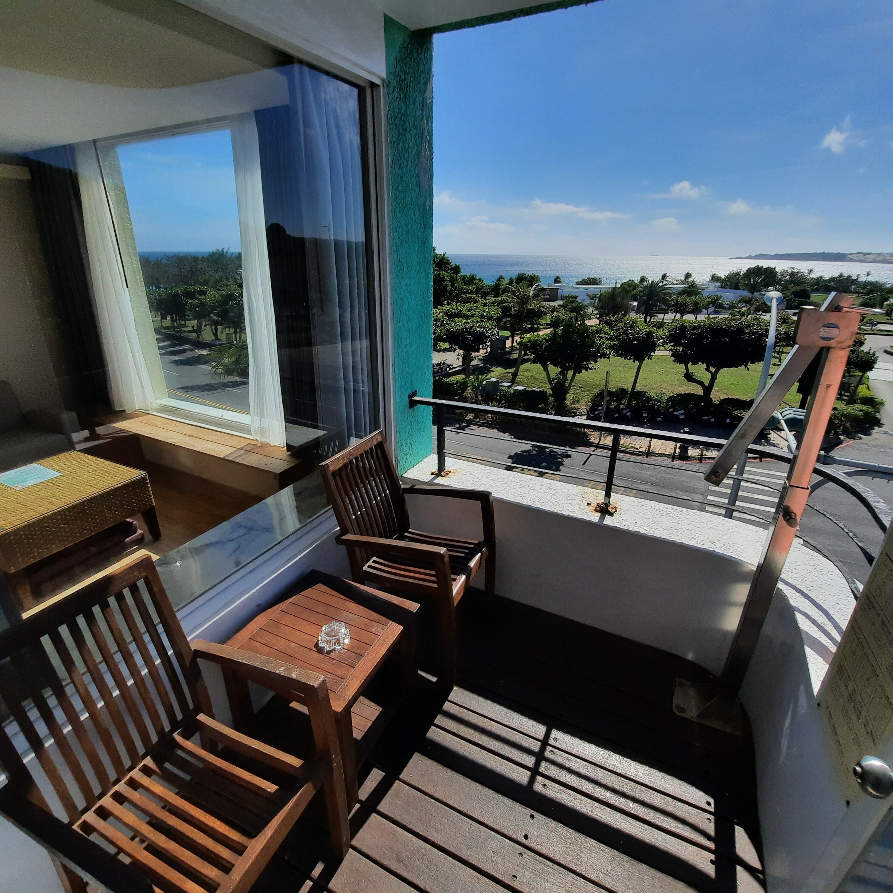 A balcony with wooden furniture, a view of the sea, and a green railing.
