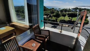 A balcony with wooden furniture, a view of the sea, and a green railing.