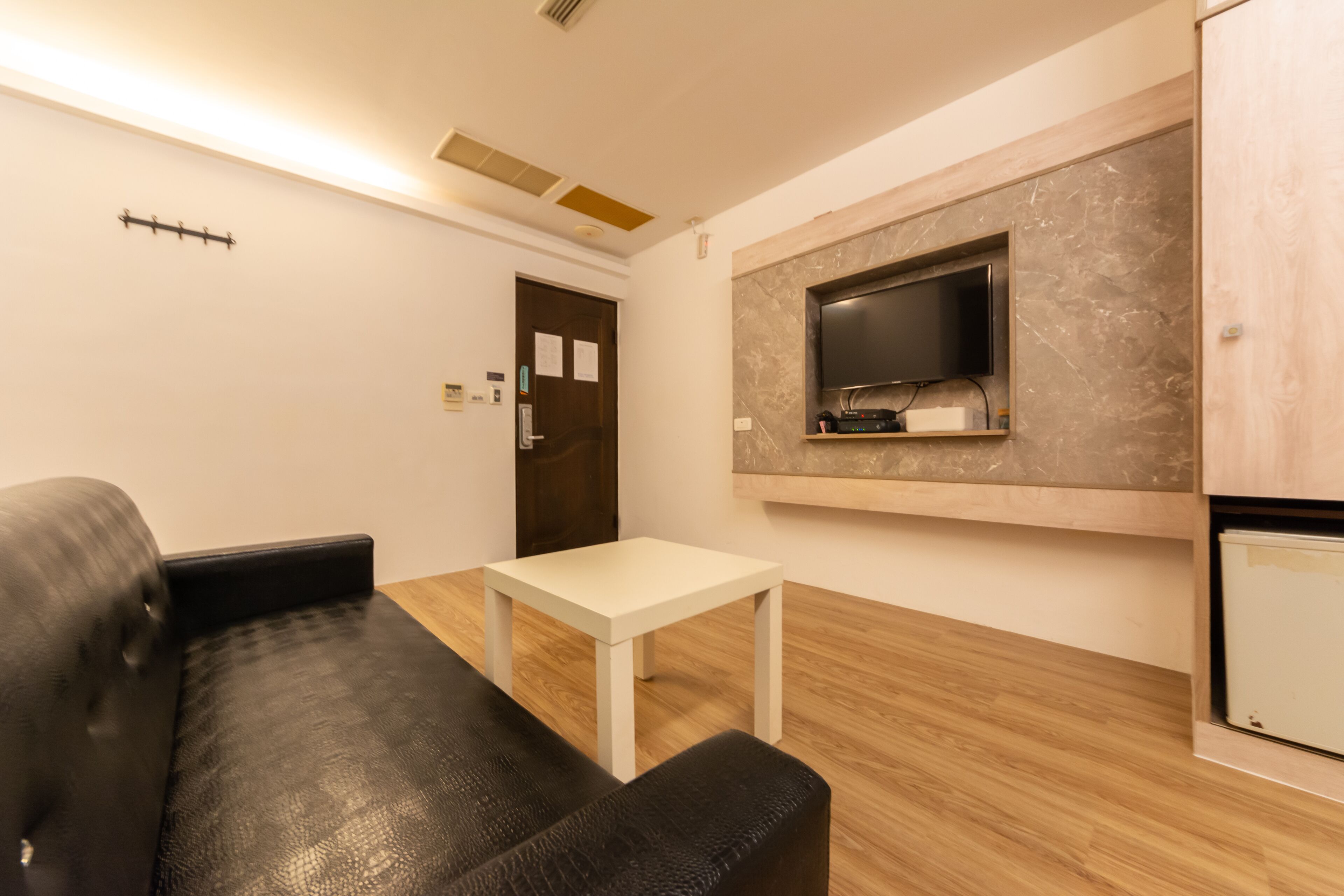 Un salón moderno con un sofá de cuero negro, una mesa blanca y un televisor montado en una pared de mármol.