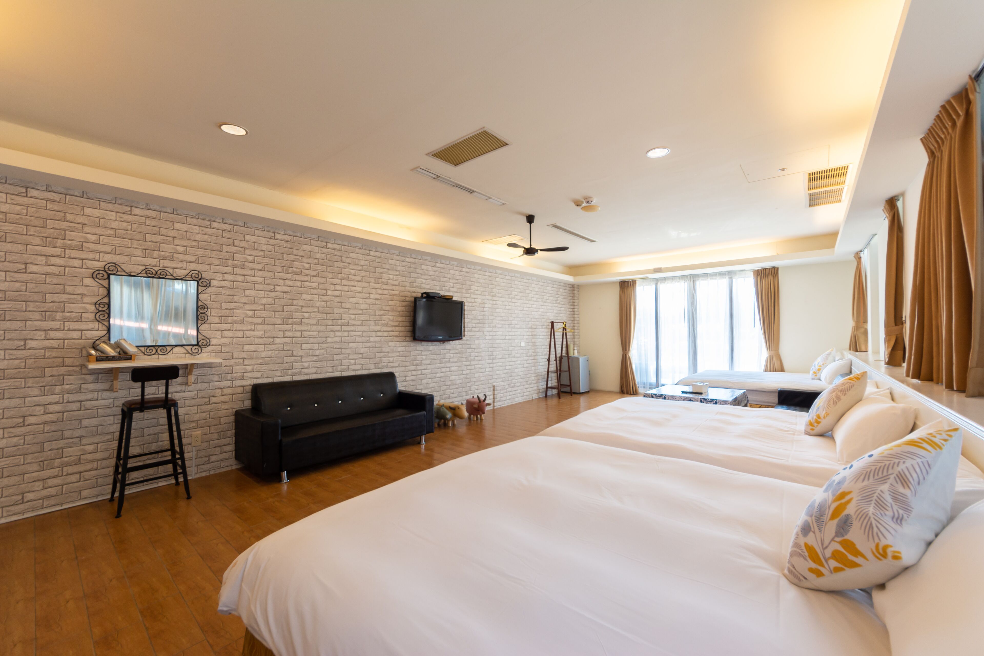 Une chambre d’hôtel avec un mur en briques, un canapé noir, un lit avec une literie blanche et un téléviseur fixé au mur.