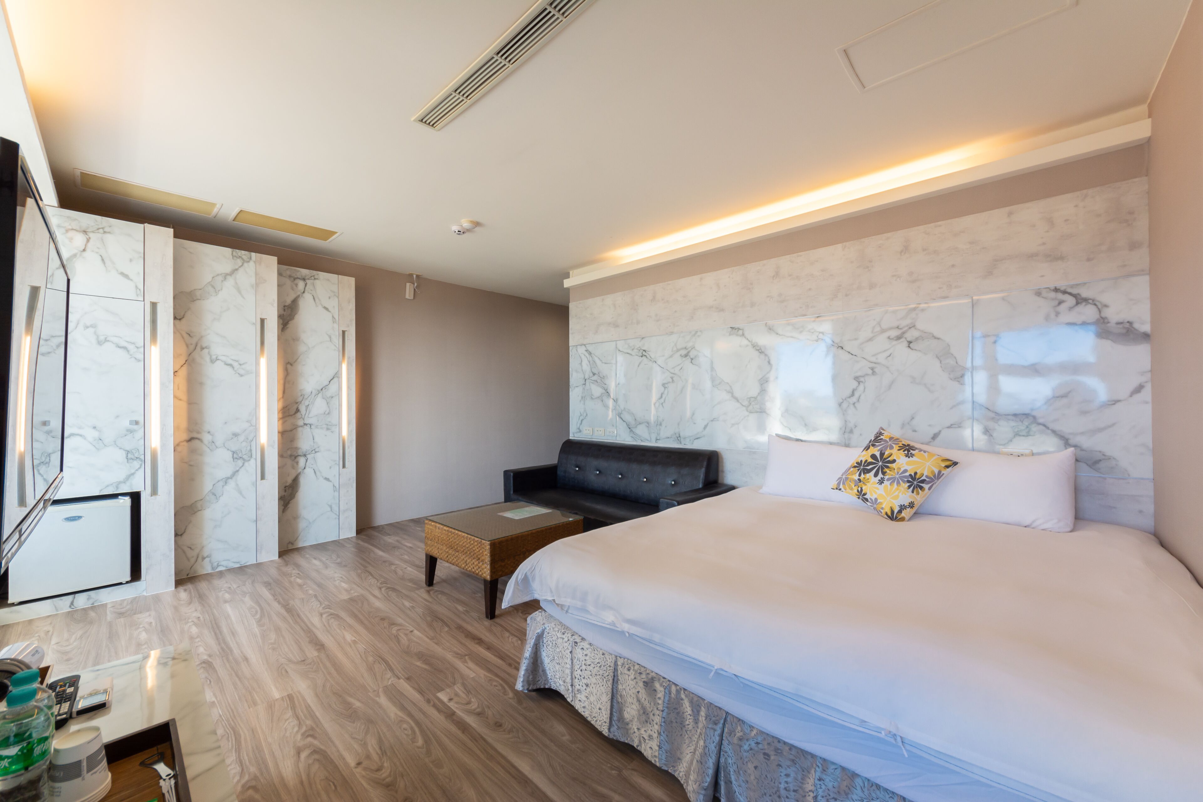 Una habitación de hotel moderna con una cama grande, un sofá, una mesita y un minibar.