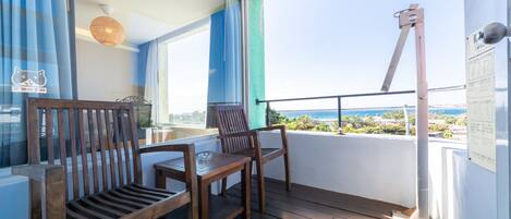 A balcony with wooden furniture, a view of the sea, and a metal structure.