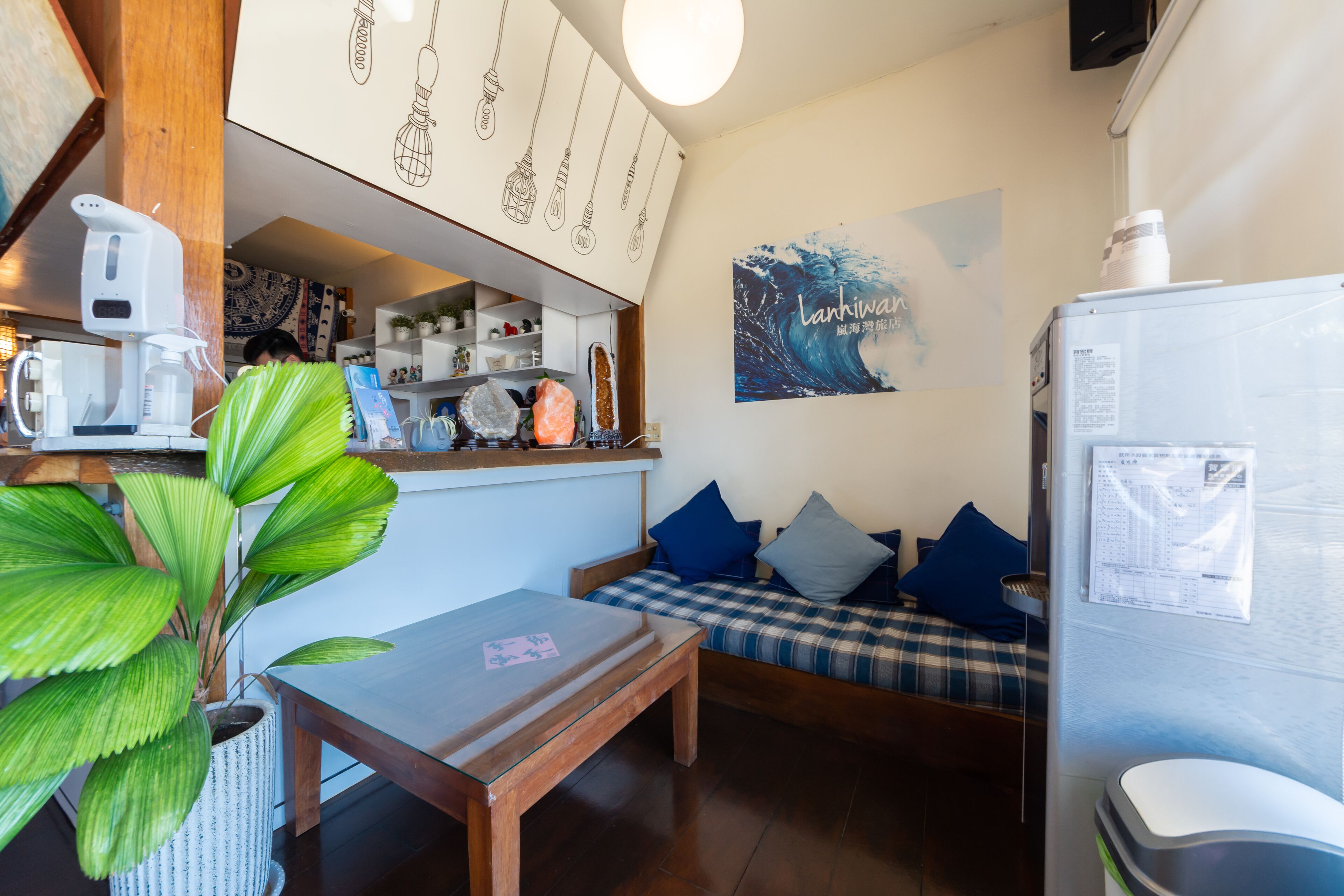 A cozy room with a sofa, a small table, a refrigerator, and a wall with a wave design.