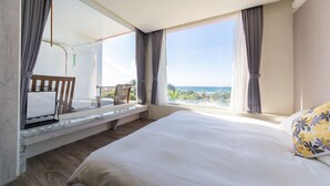 Quarto com uma cama grande, um assento junto à janela com uma cadeira e vista para o oceano.