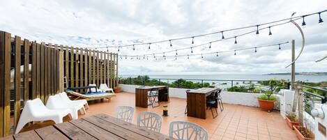 An outdoor patio with wooden tables and chairs, a wooden fence, and string lights.