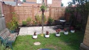 Ein Garten mit Holzzaun, einem Patio-Tisch und -Stühlen sowie mehreren Blumentöpfen.