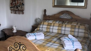 Ein hölzernes Bett mit Karo-Bettwäsche, ein an der Wand befestigter Spiegel, eine Wandteppich und ein Nachttisch mit Lampe und Tasse.