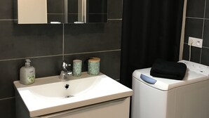 A bathroom with a white sink, a mirror, a black shower curtain, and a white washing machine. - Apartment historic center Neufchâteau (Neufchâteau)