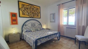 A bedroom with a bed, a chair, a nightstand, and artwork on the walls. - Fronte Mare - Facing the sea (Perd'e Sali)
