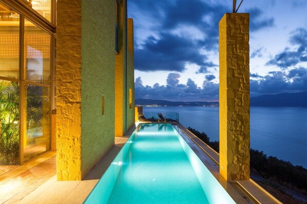 Una piscina con vistas al mar y a las montañas, rodeada de muros de piedra y puertas de cristal.