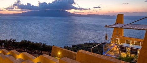 Une propriété située en bord de mer, dotée d’une terrasse avec vue sur la mer, d’un espace repas avec des sièges extérieurs et d’un escalier menant à la terrasse.