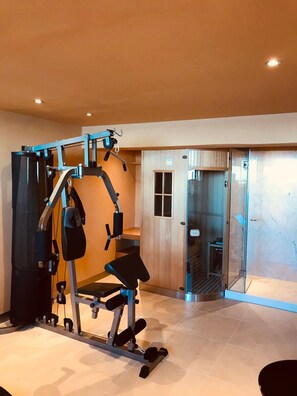 Un gimnasio con barra de dominadas, banco de pesas y puerta de cristal que da a una zona de duchas.