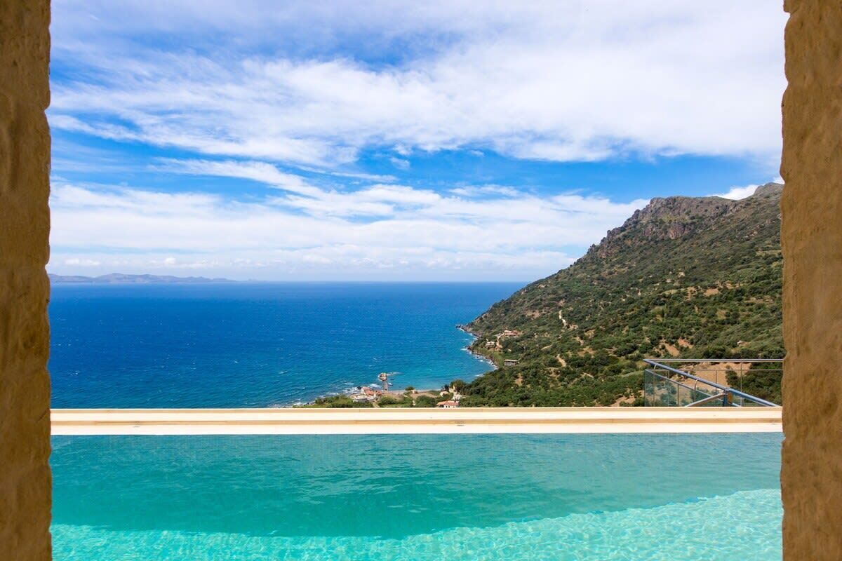 A coastal view with a clear sky, a swimming pool, and a mountainous landscape in the background.