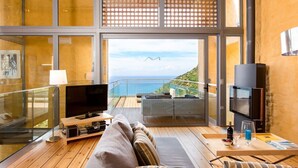 Ein modernes Wohnzimmer mit großem Fernseher, Sofa und Balkon mit Meerblick.