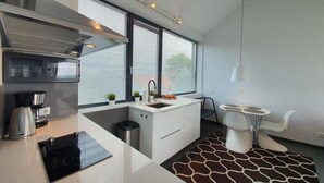 A modern kitchen with a built-in stove, a coffee maker, and a sink. There is a small dining area with a table and chairs. - Apartamenty Boulevard - 365PAM (Ustronie Morskie)