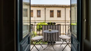 Een balkon met een tafel en twee stoelen, uitzicht op een gebouw met ramen, en een hanglamp.