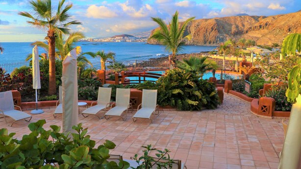 Zona junto a la piscina con sillones de descanso, piscina y vistas al océano y montañas.