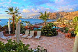 Zona junto a la piscina con sillones de descanso, piscina y vistas al océano y montañas.