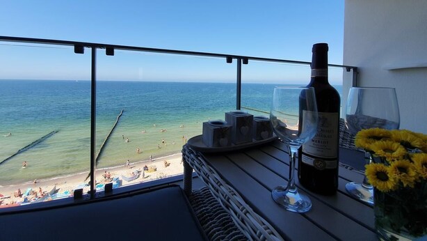 Ein Balkon mit Blick auf den Strand, eine Weinflasche, Gläser und eine Vase mit Blumen.