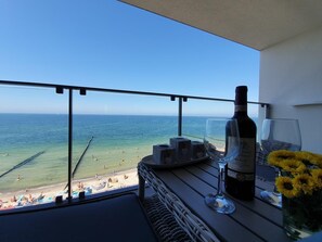 A balcony with a view of the beach, a bottle of wine, glasses, and a vase with flowers. - Apartament Sailor - 365PAM (Ustronie Morskie)