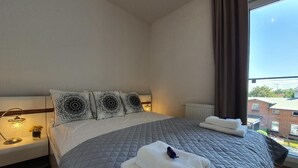 Ein ordentlich gemachtes Bett mit einer grauen Decke, zwei gemusterten Kissen und einem auf dem Bett gefalteten weißen Handtuch.
