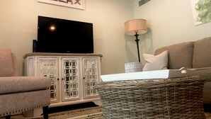 Una sala de estar con un televisor sobre un mueble, una lámpara, un sofá y un letrero decorativo que dice "RELAX".