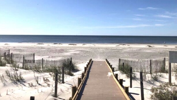 Un muelle de madera que conduce a una playa de arena con cielo despejado.