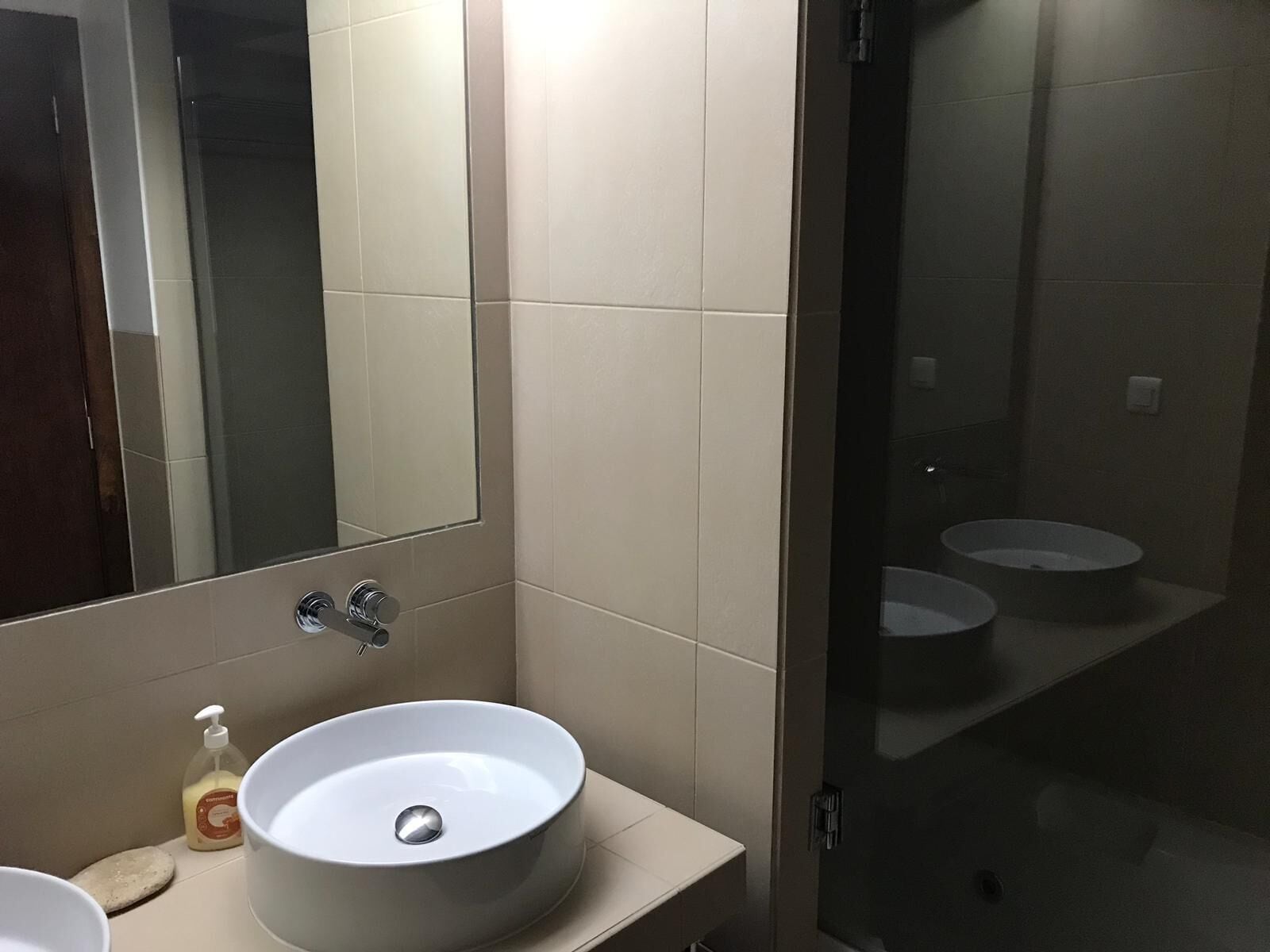 A bathroom with a large mirror, a round sink, and two smaller sinks in the background.