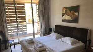 Ein Hotelzimmer mit einem großen Bett, einem Sessel, einem Bild an der Wand und Blick durch das Fenster.