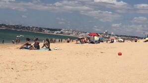 Ein Strand mit Menschen, Sonnenschirmen und einer Stadtkulisse im Hintergrund.