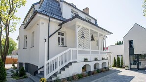 A two-story house with a white exterior, a blue roof, and a front porch with a white railing. - Apartamenty Stella Mare - 365 PAM (Ustronie Morskie)