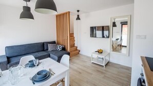 A modern living room with a grey sofa, a dining table set with plates and glasses, and a staircase leading to another level. - Apartamenty Stella Mare - 365 PAM (Ustronie Morskie)
