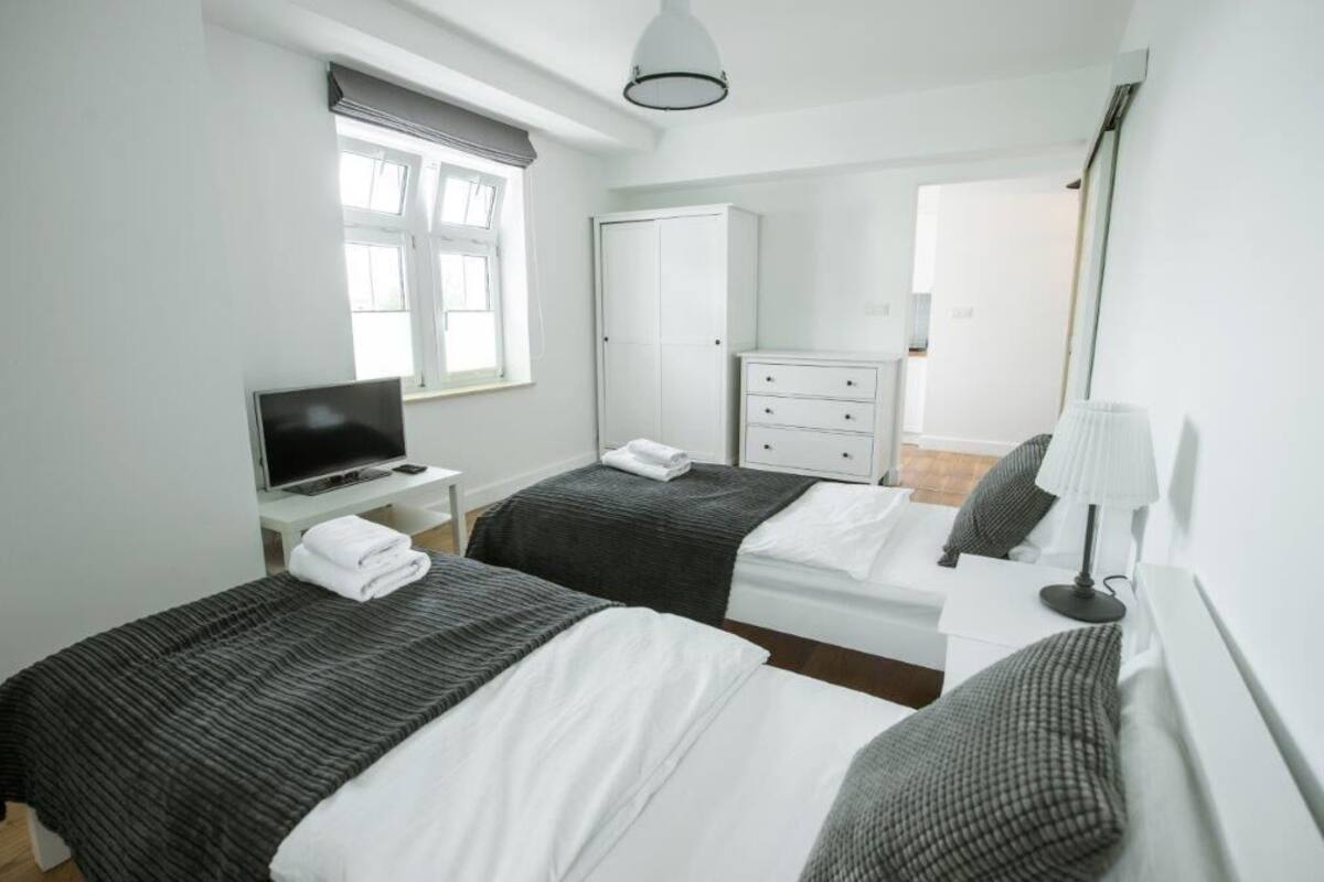 Ein modernes Hotelzimmer mit zwei Betten, einem Fernseher, einem Kleiderschrank und einem Schreibtisch mit Lampe.