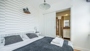 A neatly arranged bedroom with a large bed, a bedside table, a lamp, and a door leading to a bathroom. - Apartamenty Stella Mare - 365 PAM (Ustronie Morskie)