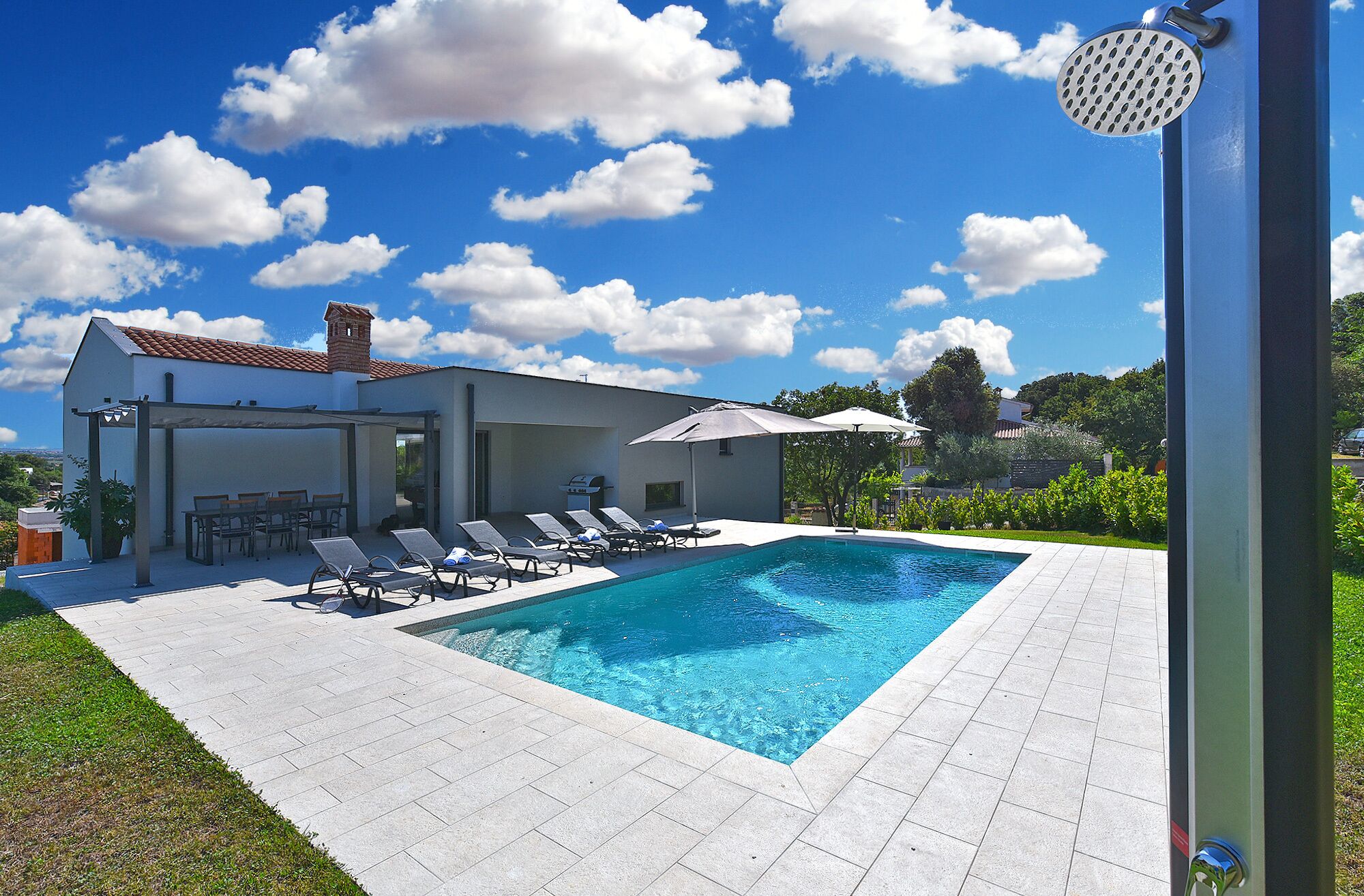 A modern house with a swimming pool, outdoor seating, and a clear blue sky.