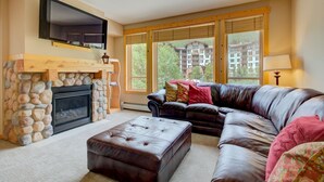 Ein Wohnzimmer mit Kamin aus Stein, einer Ledersofa und großen Fenstern mit Jalousien.