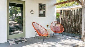 Ein Haus mit grüner Tür, zwei orangefarbene Drahtstühle, einem kleinen Tisch mit einer Vase und einem Holzzaun.