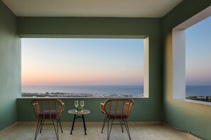 Un balcón con dos sillones de mimbre y una mesita pequeña, con vistas a la costa durante el atardecer.