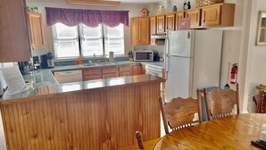 A kitchen with wooden cabinets, a refrigerator, a microwave, and a dining area with a wooden table and chairs.