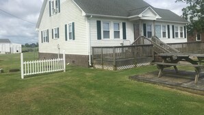 A white two-story house with a grey roof, a wooden deck, and a white picket fence.