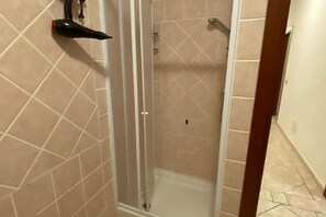 Een douche met een glazen deur, beigekleurige betegelde wanden en een witte vloer.