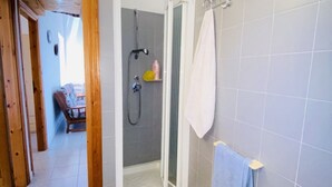 Ett badrum med dusch, en vit handduk och en liten hylla med toalettartiklar.