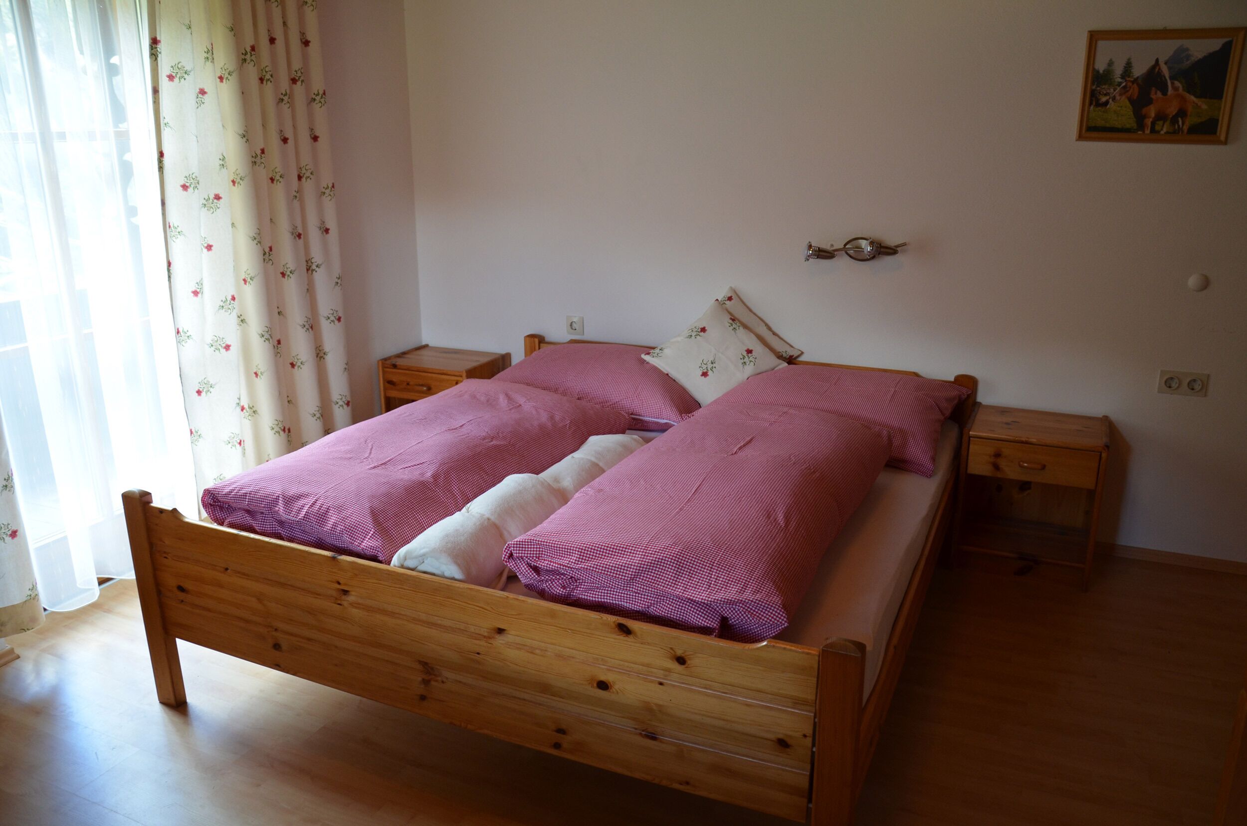 A wooden bed with two pillows, a bedside table, and a wall-mounted light fixture.