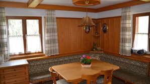 Un comedor con mesa de madera y bancos, ventilador de techo y ventana con cortinas.