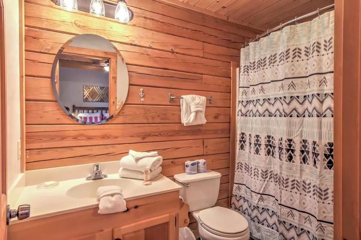 A wooden cabin bathroom with a round mirror, a sink, a toilet, and a shower curtain.